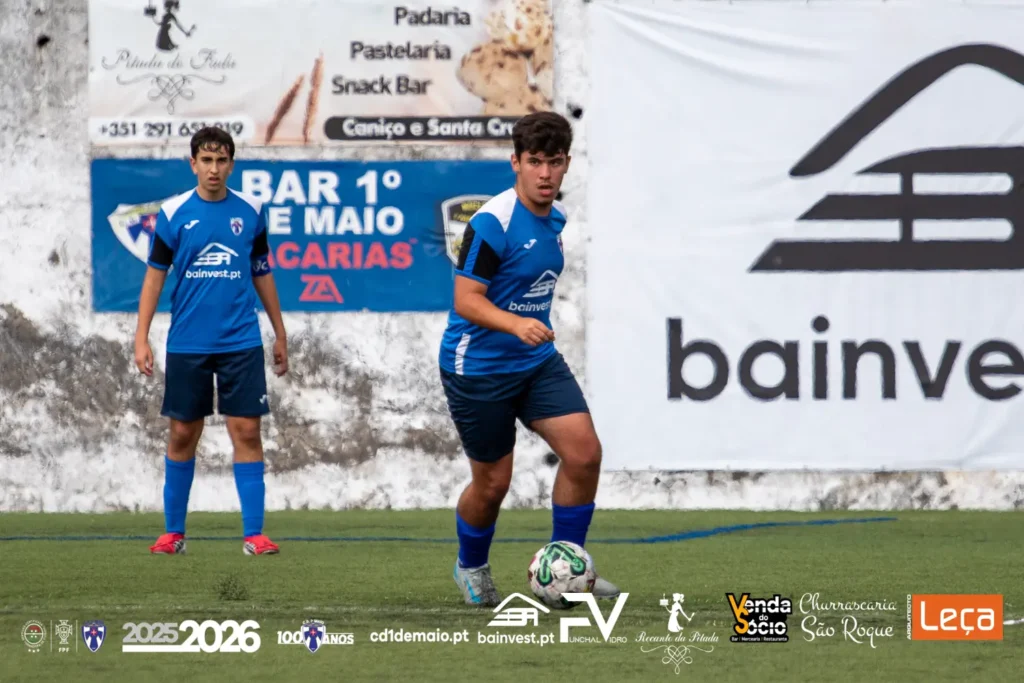 Jogadores de Juvenis Sub-16 do C.D. 1º de Maio, escola de futebol na Madeira, equipados com camisola azul e branca, perfilados em campo na época 2025/2026.